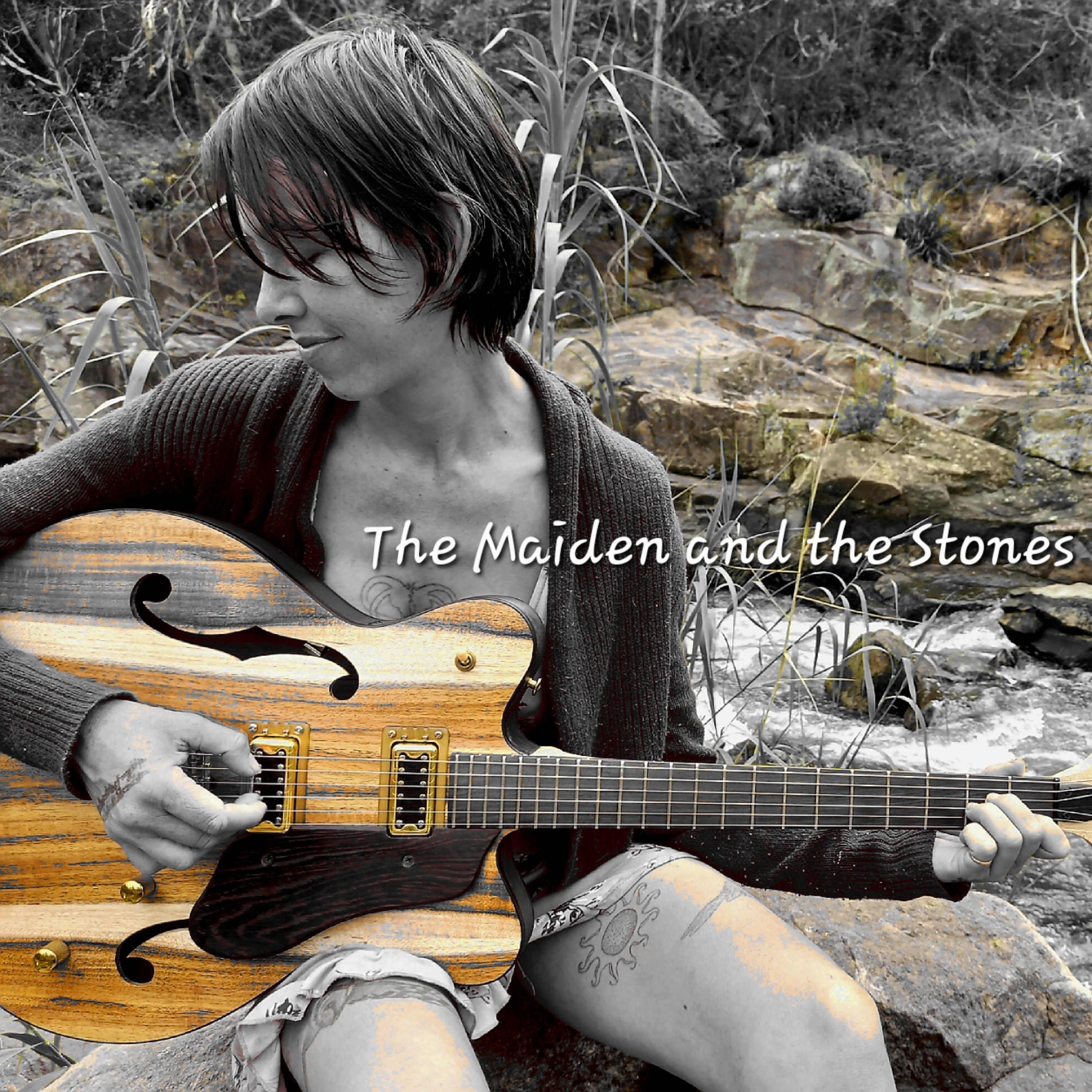 Artist with a guitar sitting by some rocks